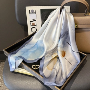 Detail of silk square scarf with blue and orange floral print on a black tray