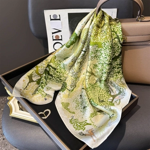 Green silk square scarf with forest deer print draped elegantly on a designer handbag