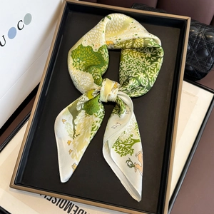 Close-up of silk twilly scarf with green forest and deer prints on a luxury display