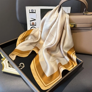 Elegant champagne silk square scarf with geometric patterns on a black display tray