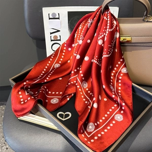 Dettaglio di un foulard in seta rossa con motivi floreali e spilla a forma di cuore