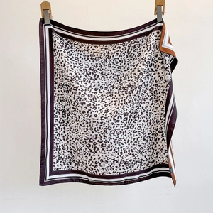 Detailed view of leopard print silk scarf with striped borders hanging on white background