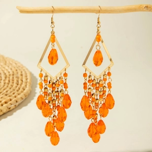 Close-up of bohemian orange beaded tassel earrings hanging on a natural wooden branch