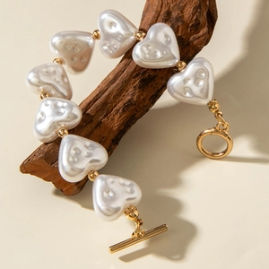 Golden toggle clasp bracelet featuring eight white heart-shaped pearls on rustic wood