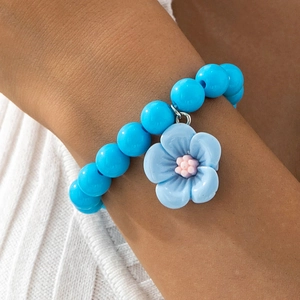 Vue détaillée d'un bracelet en perles bleues avec pendentif fleur en résine au poignet