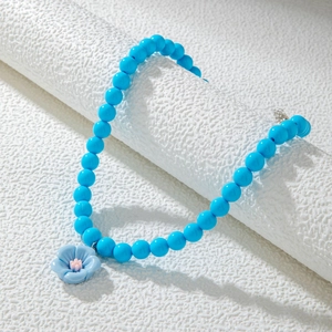 Détail de collier en perles bleues avec pendentif camélia bleu et cœur de fleur rose