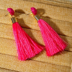 Gros plan détaillé de boucles d'oreilles à pompons fuchsia avec clous ronds tressés