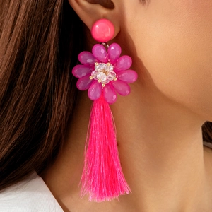 Détail de boucles d'oreilles bohèmes roses avec fleurs, perles et longs pompons