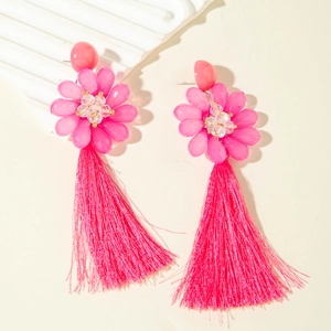 Gros plan sur des boucles d'oreilles fleurs en raphia rose vif à longues franges
