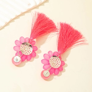 Détail macro de boucles d'oreilles fleur fuchsia avec de longs glands en soie sur fond beige