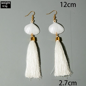 Détail de boucles d'oreilles à pompons blancs avec coquillage et mesure de 12 cm de long