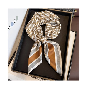 Detailed close-up of a silk scarf with gold chain patterns tied in a bow on a tray