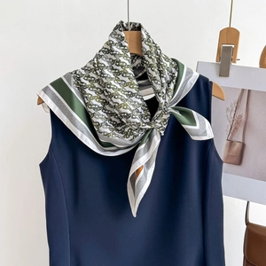 Olive green chain print silk scarf draped on a wooden hanger with minimalist decor