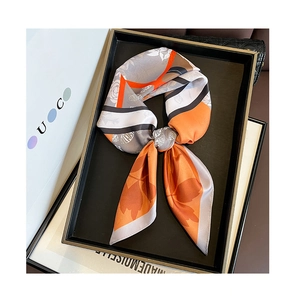 Detailed view of an orange and grey floral twill silk scarf tied in a black gift tray