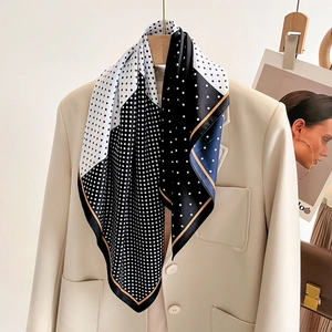 Polka dot silk scarf in black and white with orange trim draped over a beige blazer