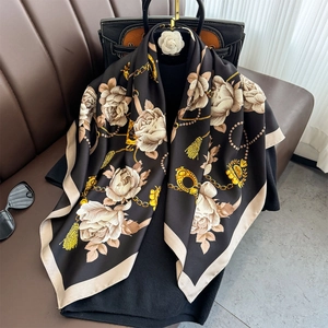 Détail d'un foulard en soie à motif camélia et chaîne drapé sur un sac à main en cuir