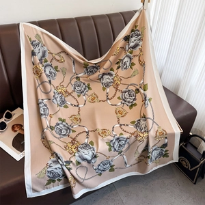 Détail d'un foulard en soie aux motifs de camélia et chaînes drapé sur un canapé en cuir