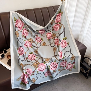 Détail d'un foulard en soie à motif camélia et chaîne dorée sur un canapé en cuir