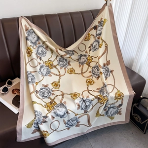 Détail d'un foulard en soie à motif camélia et chaîne dorée sur fond de cuir