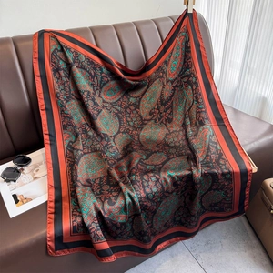 Large paisley print silk shawl in burnt orange and black on a leather sofa surface