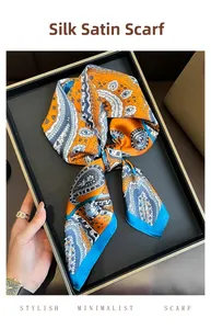 Detail of orange and blue paisley silk satin square scarf folded on a black tray