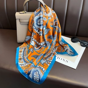 Classic paisley print satin silk scarf in orange and peacock blue draped over a handbag