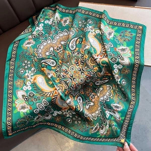 Detailed close-up of emerald green paisley silk scarf draped on a leather surface
