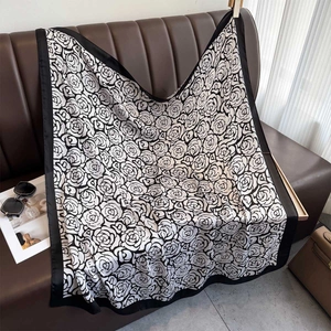 Grande foulard quadrato in seta con stampa di camelia e bordo nero su divano in pelle
