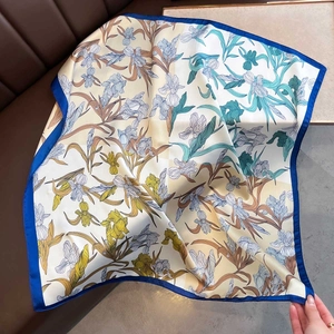 Detail of silk-like floral square scarf showing blue iris patterns and hemmed edges