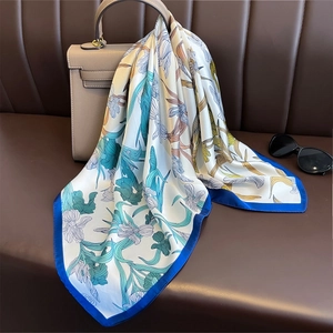 Silk-like floral scarf with iris pattern draped over a beige handbag on a leather sofa