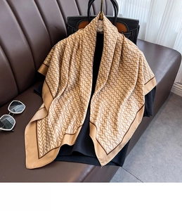Detail of premium silk square scarf with geometric V-pattern over brown fabric background