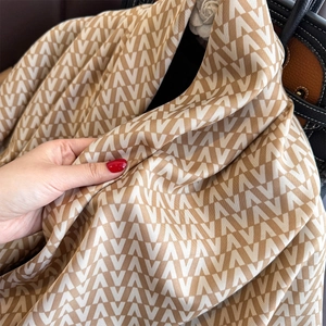 Detail of luxury silk scarf with V-letter jacquard pattern draped over black handbag
