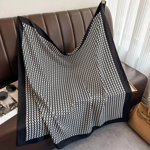 Detailed view of luxury square scarf with black and white V-pattern on leather sofa