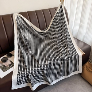 Detail of a square silk scarf with black and white V-pattern draped on a leather sofa