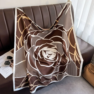 Detail of silk-satin square scarf with brown floral pattern draped on a leather sofa