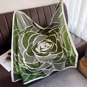 Detail of silk scarf with green rose print draped on sofa with chic travel accessories