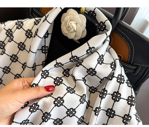 Nahaufnahme eines schwarz-weißen Seidenschals mit Blumenmuster und einer Kamelien-Brosche