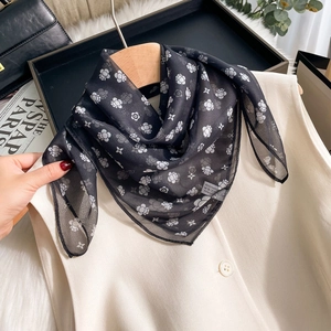 Elegant black silk chiffon scarf featuring white floral patterns on a wooden hanger