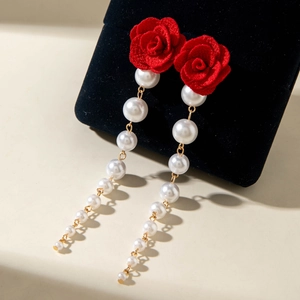 Detail of red fabric rose earrings with elegant pearl tassel on black velvet stand