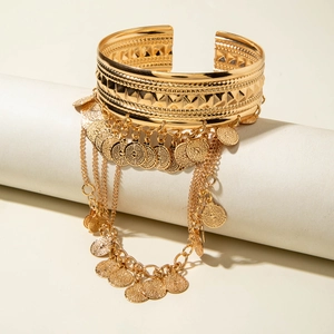 Détail d'un bracelet manchette doré avec relief géométrique et pampilles de pièces en chaîne