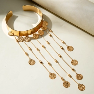 Détail d'un bracelet de bras doré avec de longues franges et des breloques texturées