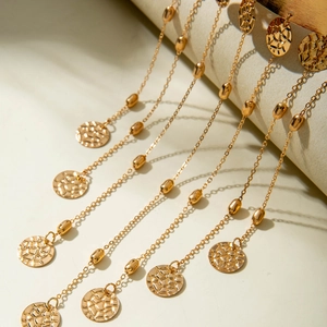 Détail de la chaîne de bras dorée avec perles et pendentifs sur décor minimaliste