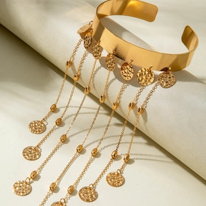 Détail de manchette de bras dorée avec franges métalliques et breloques de pièces gravées