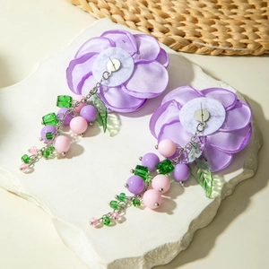 Macro shot of purple fabric camellia earrings with green leaf beads and colorful tassels