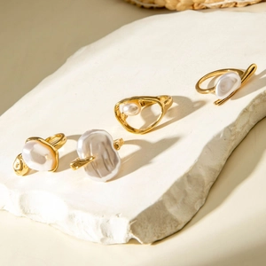 Artistic detail of four baroque pearl rings in gold finish on textured stone surface