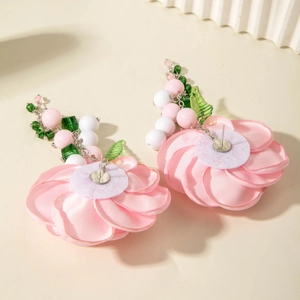 Detail view of pink fabric camellia earrings with green leaf and bead tassels