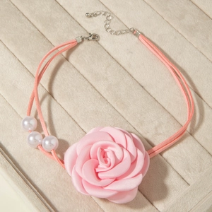 Detail of pink satin fabric rose choker with white pearl accents on beige velvet tray