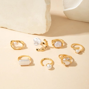Set of seven gold-tone baroque pearl rings displayed on a textured stone surface