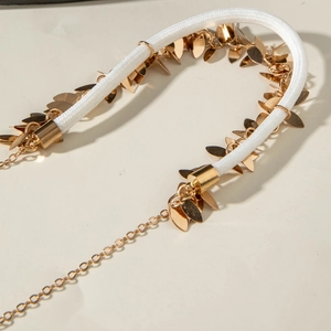 Macro detail of golden metal leaf charms on white braided rope statement necklace