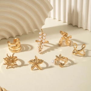 Set of 7 gold rings with pearls, starfish and sun patterns on a white textured background